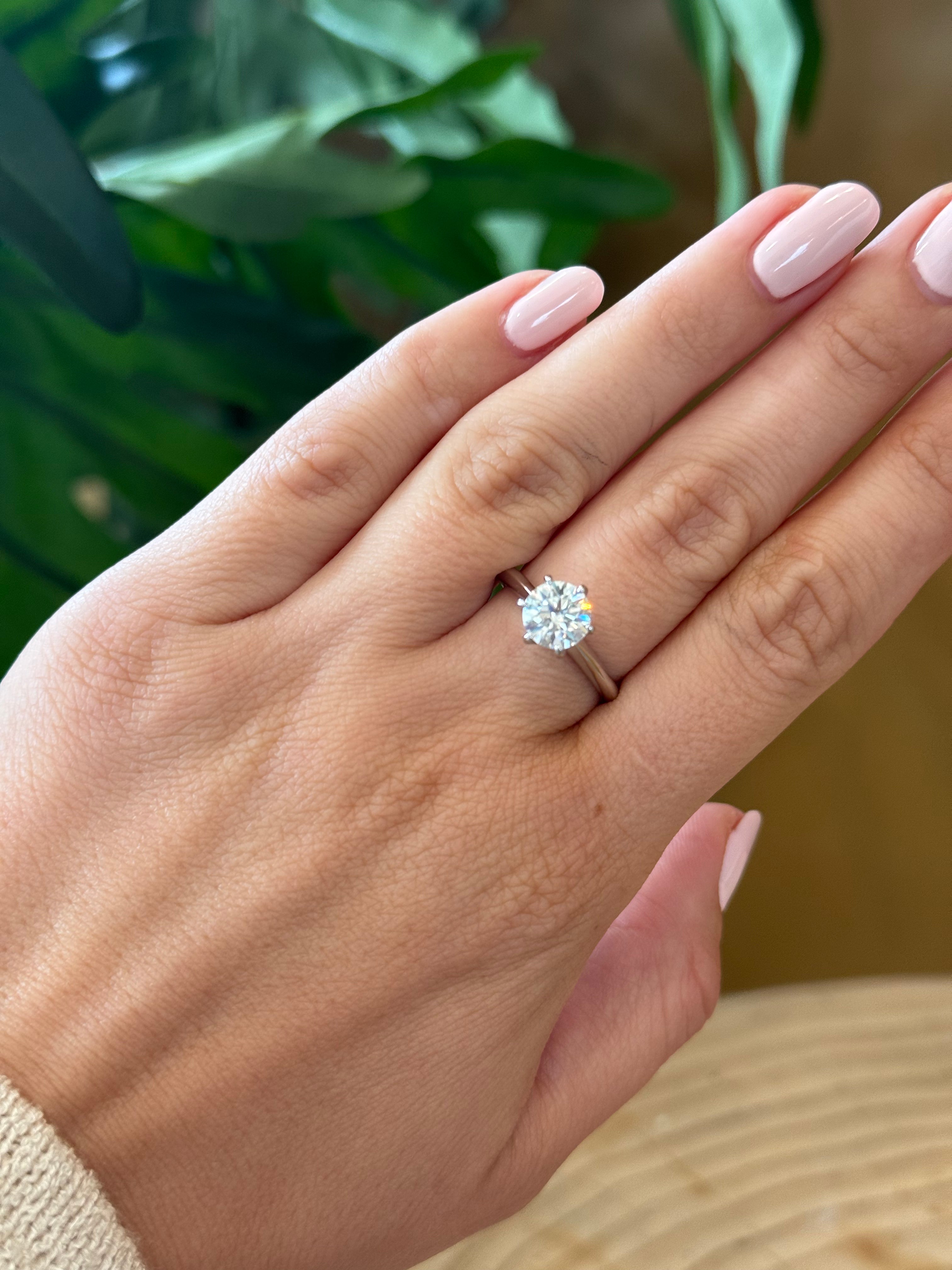 Hand wearing a diamond ring with a blurred green plant background