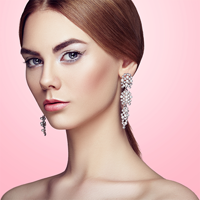 Elegant woman with long hair and sparkling earrings against a pink background, showcasing beauty and glamour.