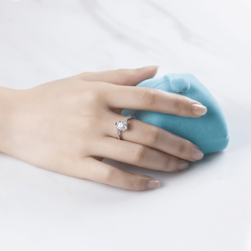 Hand showcasing The Callista ring with stunning 1.0CT moissanite on a soft blue pillow. Perfect for engagements and weddings! 💍✨