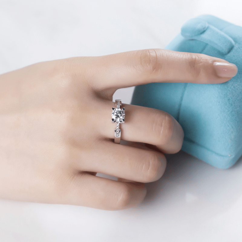 Hand wearing The Celestara ring with 1.0CT moissanite, showcasing elegance next to a blue ring box 💍✨