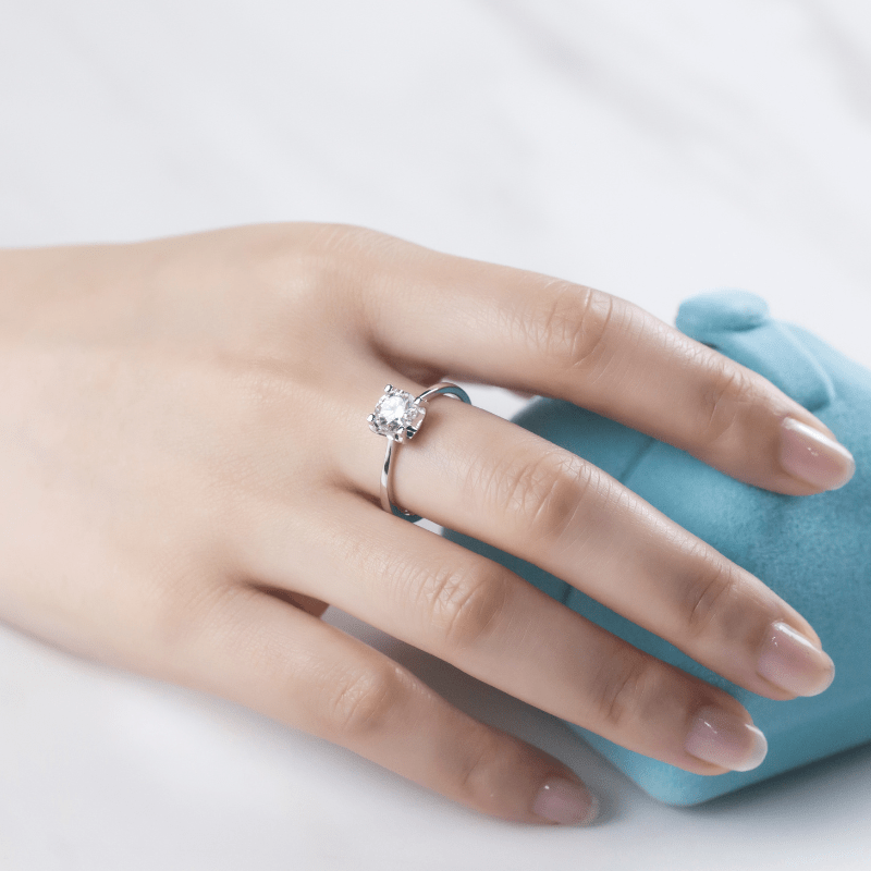 A hand showcasing The Estelle Moissanite Solitaire Engagement Ring 1CT on a blue ring box. 💍✨ #Engagement #Moissanite