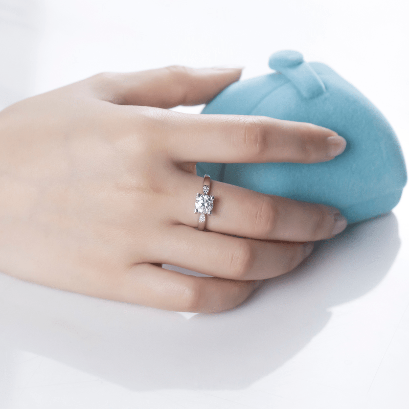 Elegant hand showcasing The Seraphine Moissanite engagement ring 💍 in a soft blue jewelry box. Stunning 1CT brilliance!